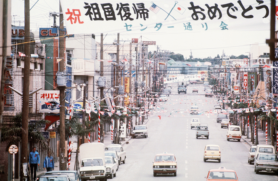 Okinawa on May 15, 1972, the day of its reversion to Japan. Displayed above the road is a banner celebrating the occasion. Under U.S. administrative control and for a while thereafter, cars drove on the right side of the road, but from 1978 onward they switched to the left in accordance with national traffic rules. Changing everything from traffic signals to signs and road markings was an enormous undertaking.  THE YOMIURI SHIMBUN/AFLO
