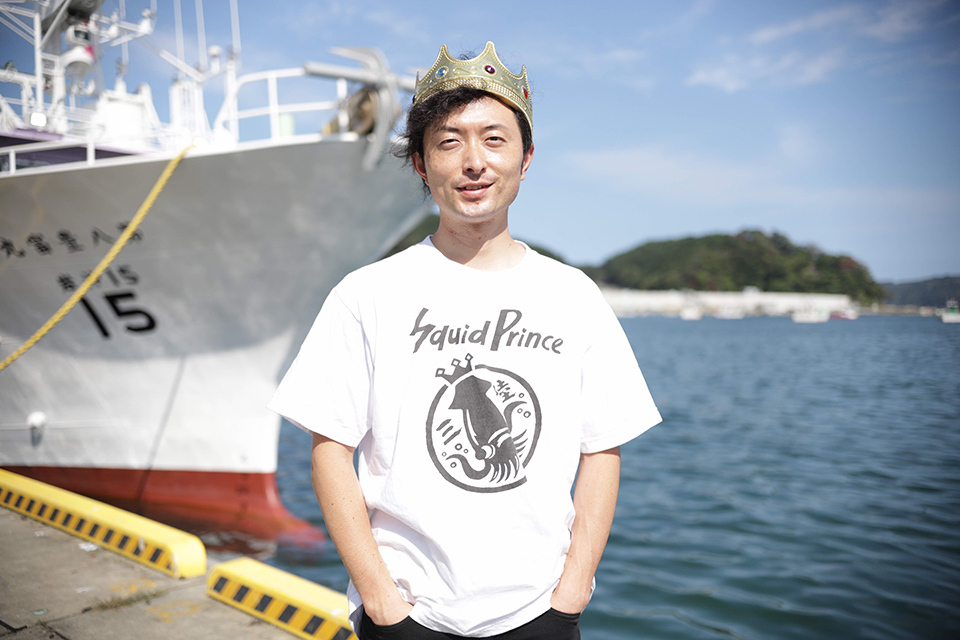 Ryota Suzuki, who works for a fish processing company in Miyako, stands wearing a crown with a fishing boat in the background.
