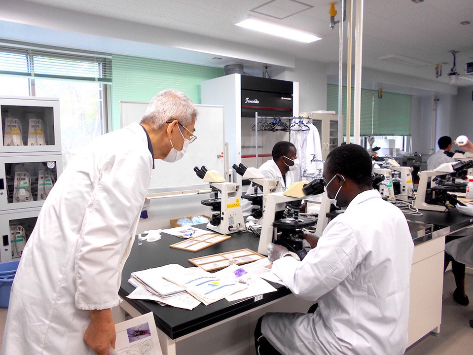 A black man looking into a microscope and a Japanese watching him.