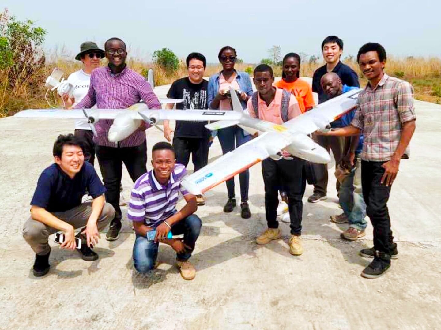 People posing for a group photo holding two fixed-wing, airplane-like, type drones in Sierra Leone.