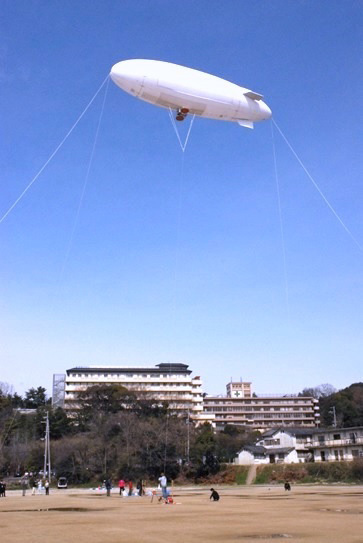 A white airship floating above an outdoor campus playground during an experiment.