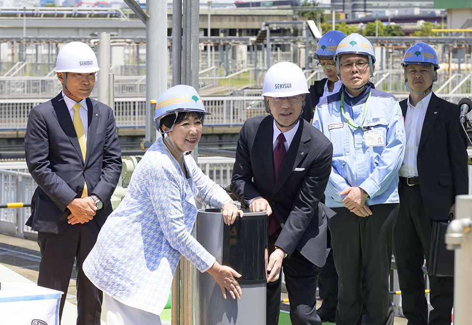 Tokyo Governor Koike and an official, surrounded by other officials, presenting a film-like solar cell wrapped around a pipe.