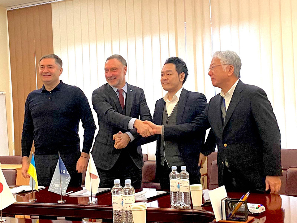 Four people standing behind a conference table, shaking hands to celebrate a contract signing. NIPPON KOEI CO., LTD.