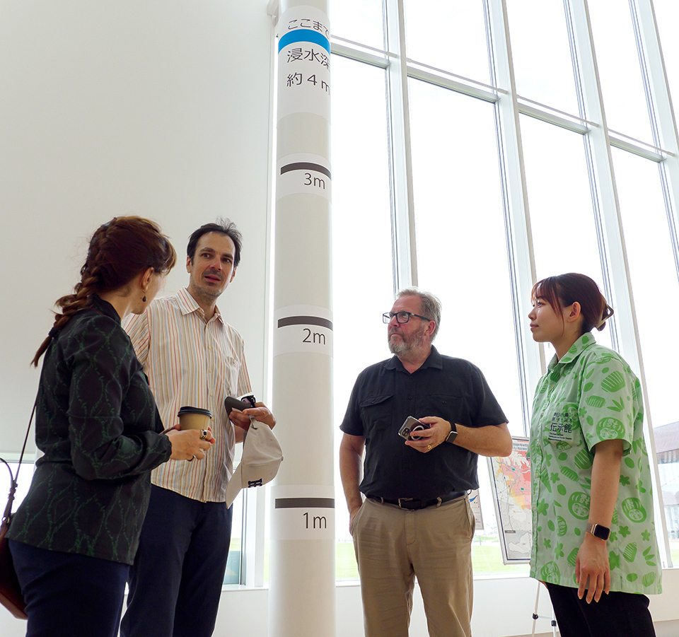 Visitors and Endo Miku standing in front of a pillar that shows the height tsunami reached.