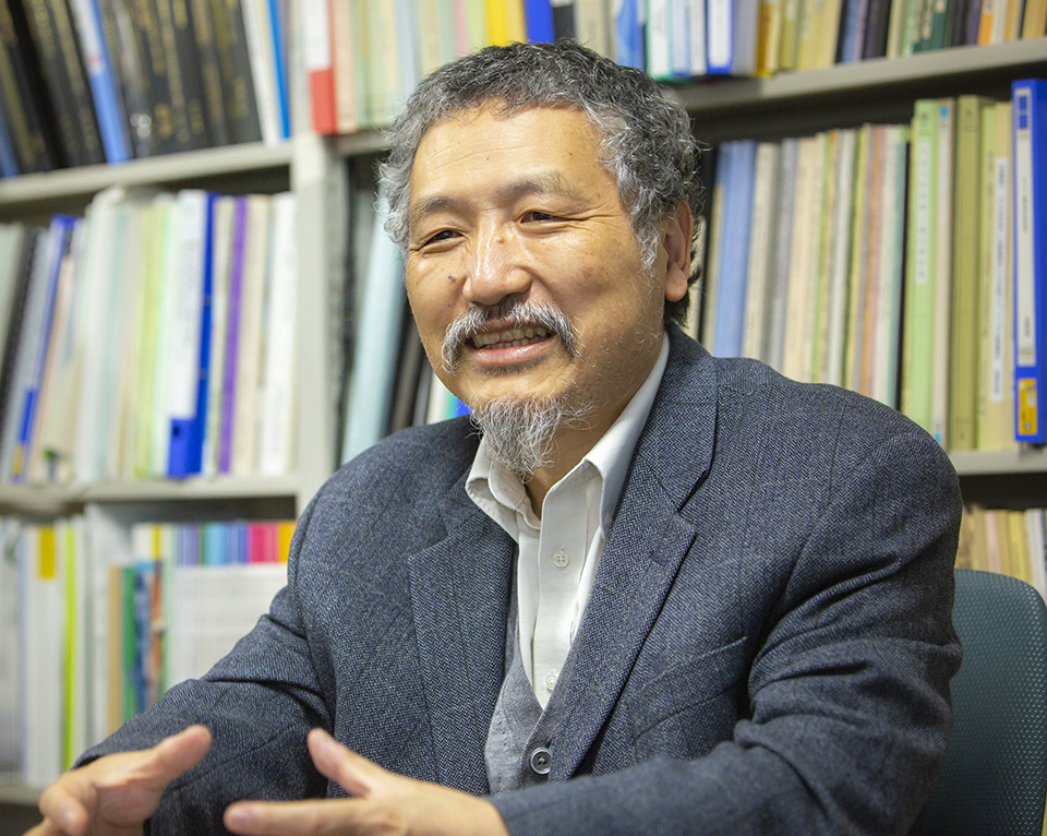 Professor Koji Okamoto of the Graduate School of Engineering, the University of Tokyo, with bookshelves with many documents in the background.