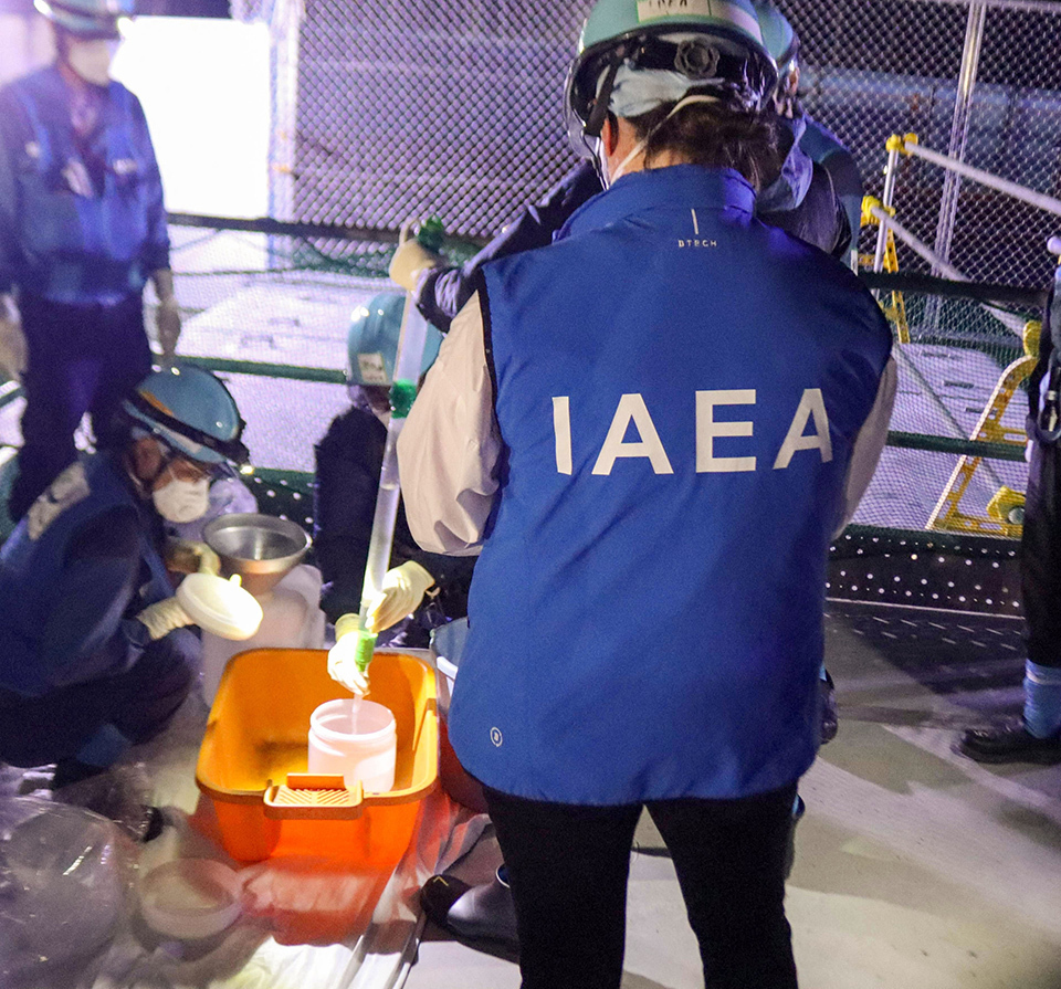 IAEA personnel wearing blue jacket at the Fukushima Daiichi Nuclear Power Station, witnessing the sampling of water treated by ALPS and diluted with seawater.