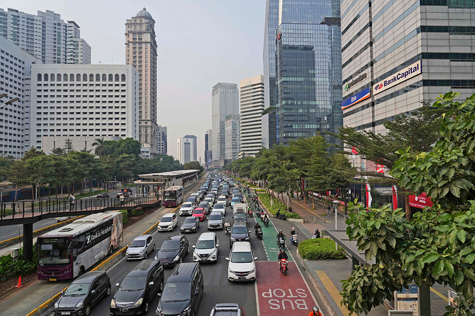 A photo of a busy city street with many cars and buildings in Jakarta, Indonesia. The street is filled with cars, buses, and trucks.