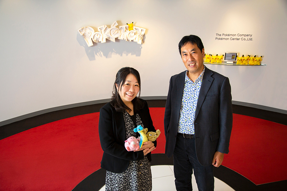 HIROSE Chihiro and SUGA Daigorotoyohide from The Pokémon Company standing in front of a wall with a white sculpture and yellow Pokémon figures on the wall.