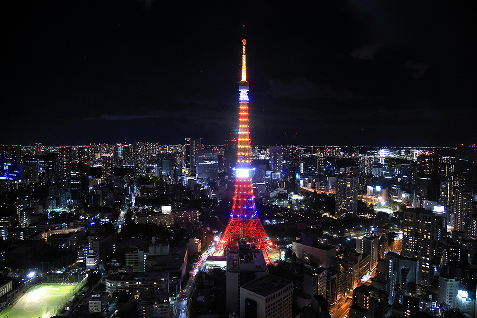 A night view of Tokyo Tower brilliantly illuminated in the vibrant colors of ASEAN, surrounded by the cityscape.
