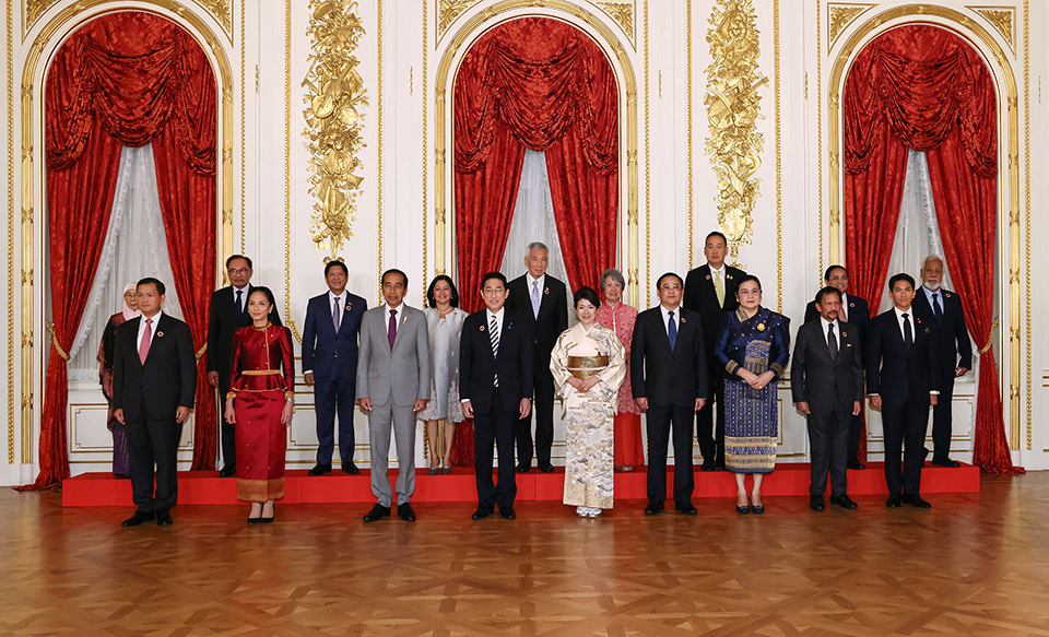 A group of people standing in a formal arrangement in an opulent room with red curtains and golden details.