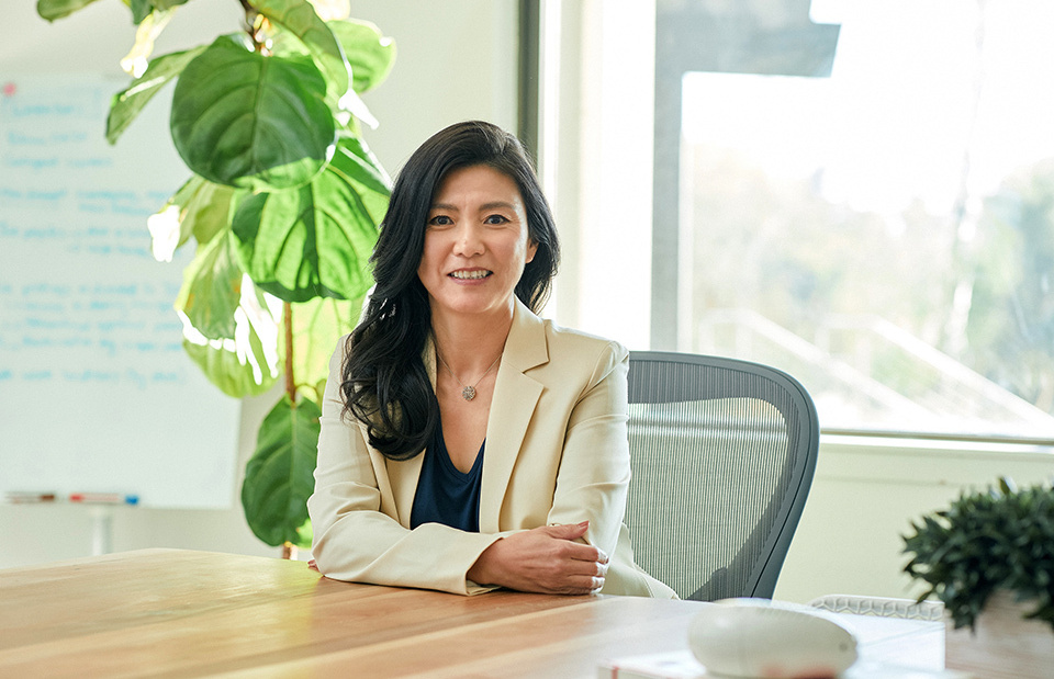MATSUOKA Yoko, the founder and CEO of Yohana, is sitting at a desk and smiling in our direction.