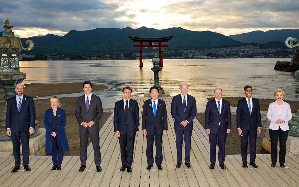 The leaders gathered at the G7 Hiroshima Summt in May 2023, lining up on a dock, with a serene sea and the floating Torii gate of Itsukushima Shrine in the background.