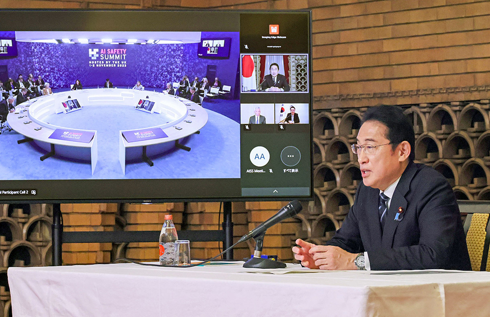Prime Minister Kishida attending online to the AI Safety Summit in November 2023, seated at a table, facing a large screen displaying other participants.
