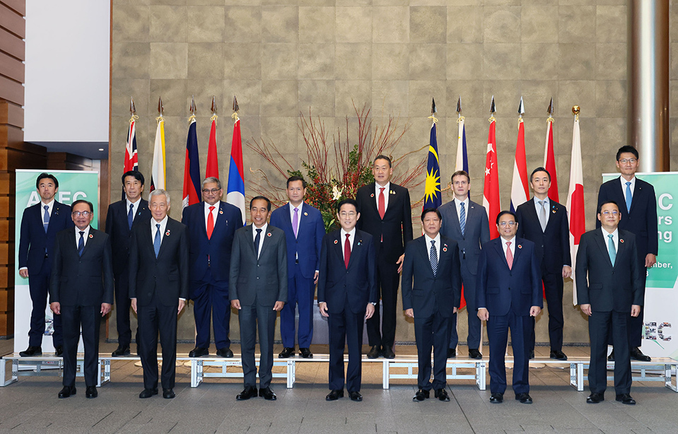 A group of leaders standing side by side, with various national flags displayed behind them and a flower arrangement centrally placed among the flags.