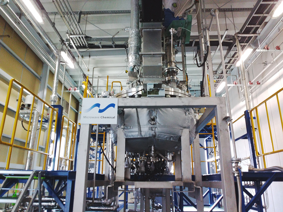 Metallic chemical unit with pipes, tanks, railings in big facility.