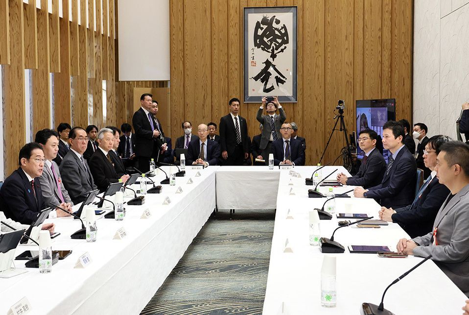 Meeting hosted by the Cabinet Office. People seated around a long rectangular table in a room with wooden walls and a calligraphy artwork hanging on the wall.