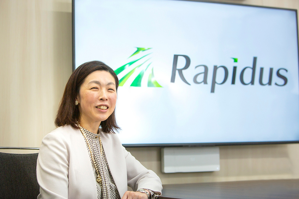 SHINDO Yukiko, senior human resources manager at Rapidus, sitting in front of a screen displaying the company logo.