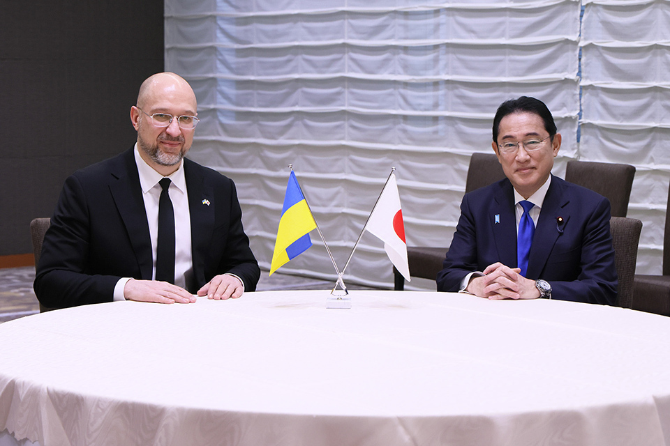 Ukrainian and Japanese Prime Minister sitting at a table, Ukraine’s and Japan's flags on the table.