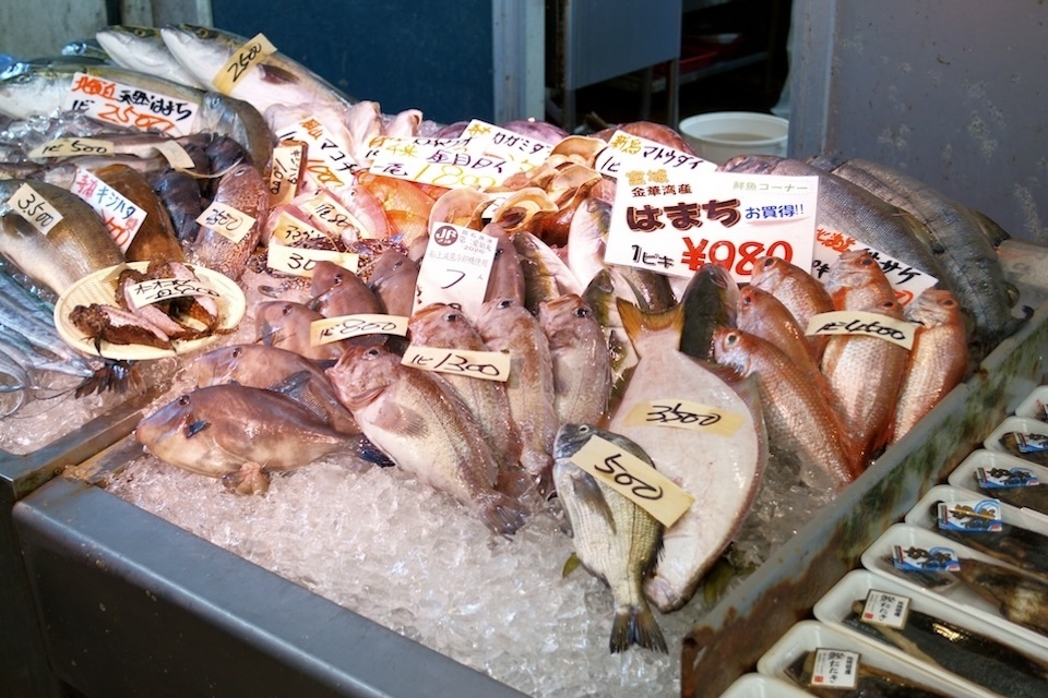 A variety of fresh fish is displayed on a bed of ice with price tags in Japanese yen.