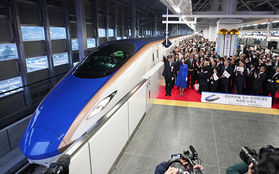 A large crowd, including people in formal attire, gathered at Tsuruga Station for the Hokuriku Shinkansen Line extension opening event.