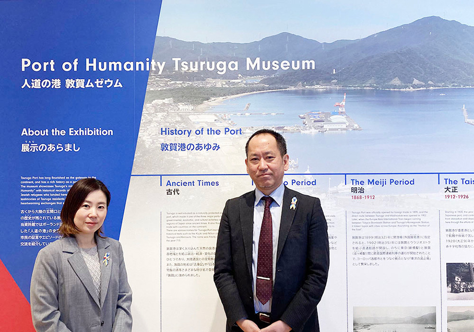 Nishikawa and Yamada standing in front of a large informational display at the Port of Humanity Tsuruga Museum.