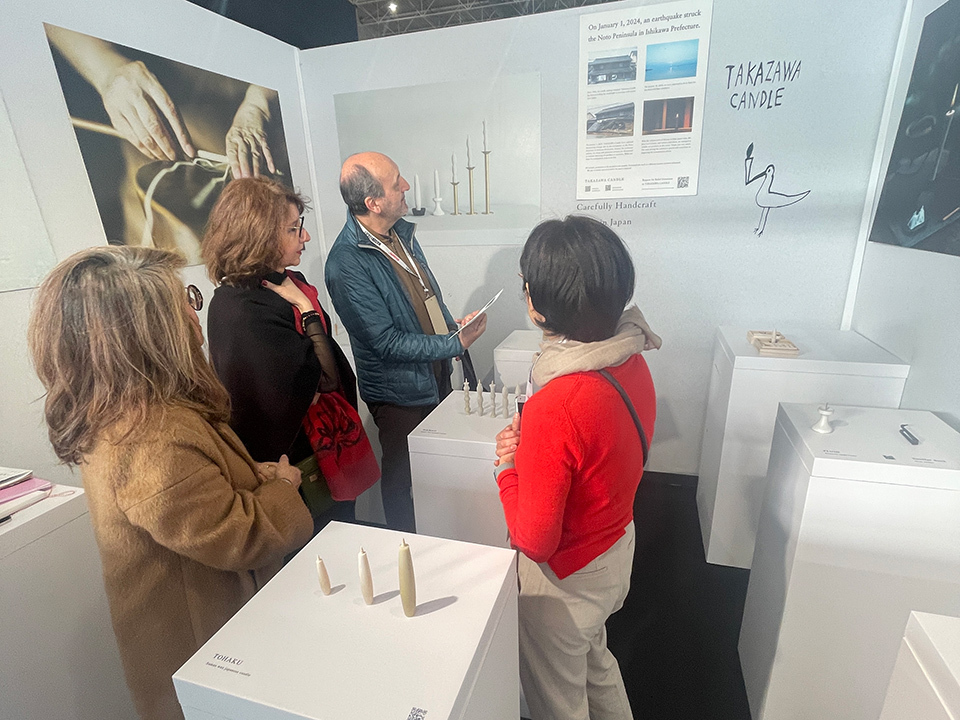 A group of four people observing various candles and informational panels in a white-walled art gallery at Maison & Objet.