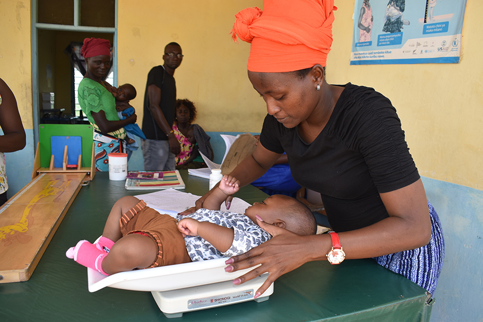 A health service volunteer weighing a baby on a scale in a clinical locating in Kenya.