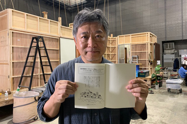 An individual holds a book open towards the camera in an indoor workshop setting.