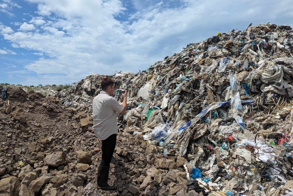 A man in a white shirt standing overlooking a landfill in Fiji and taking photos
