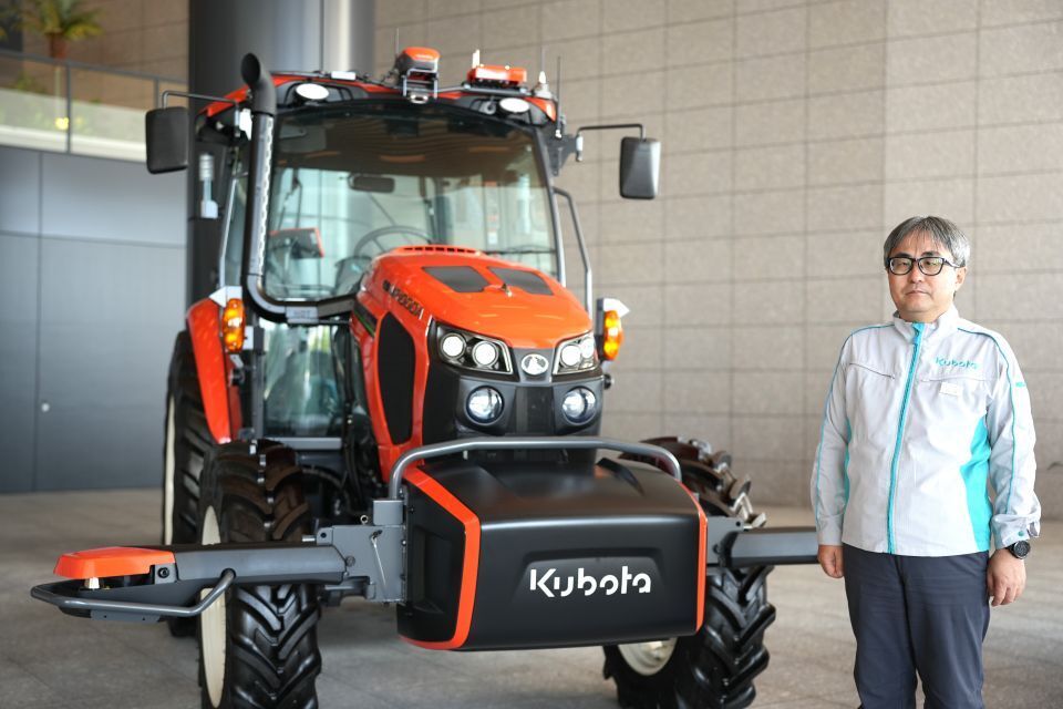 Man in a grey and blue jacket posing by a Kubota combine harvester