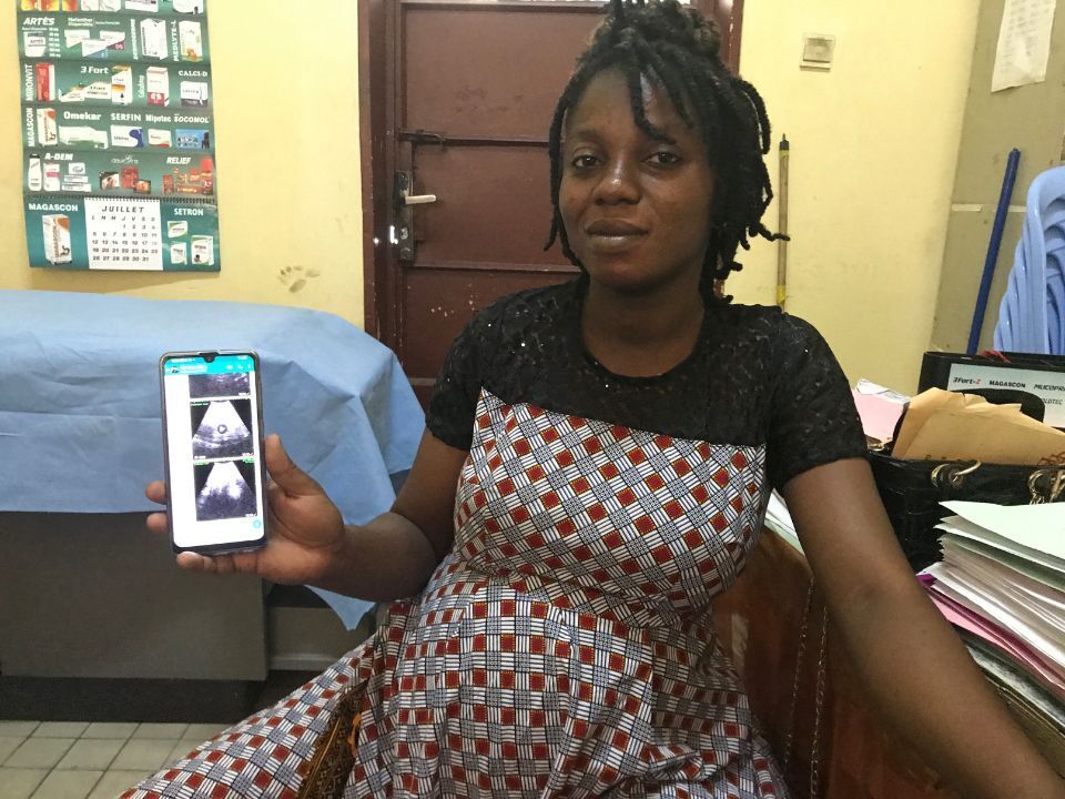 A pregrant woman with short braids showing a sonogram on a smartphone