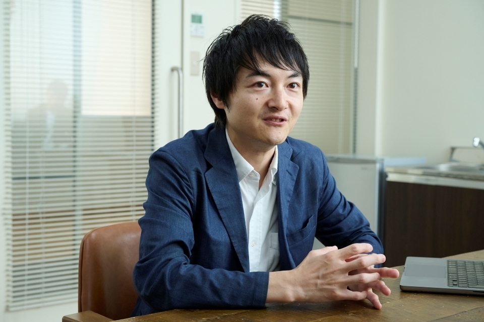 A photo of Masui Kosuke, a Japanese man wearing a blue jacket and sitting at a desk