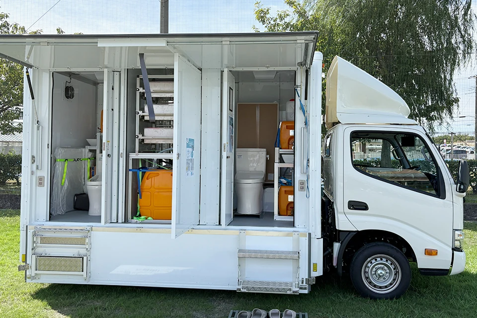 A small white truck carrying a unit with two toilets connected to an e6s system.