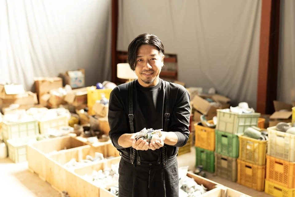 Okuyama Junichi, CEO of CACL Inc., standing in front of crates of broken pottery