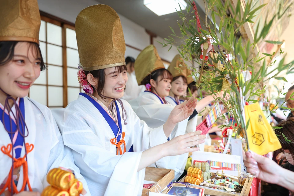 Women in traditional Japanese clothing and tall golden hats giving out bundles of bamboo at Imamiya Ebisu Shrine in Osaka