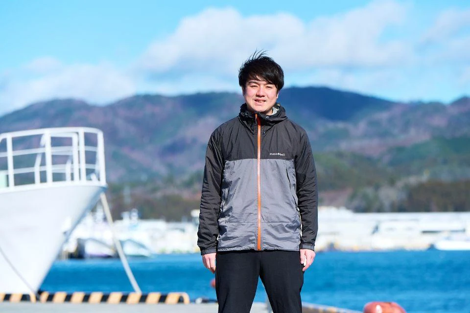 Kato Kodai, CEO of amu inc., standing in front of boats in Kessennuma harbor