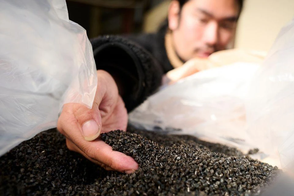 Man scooping up dark nylon pellets, made from recycled fishing nets