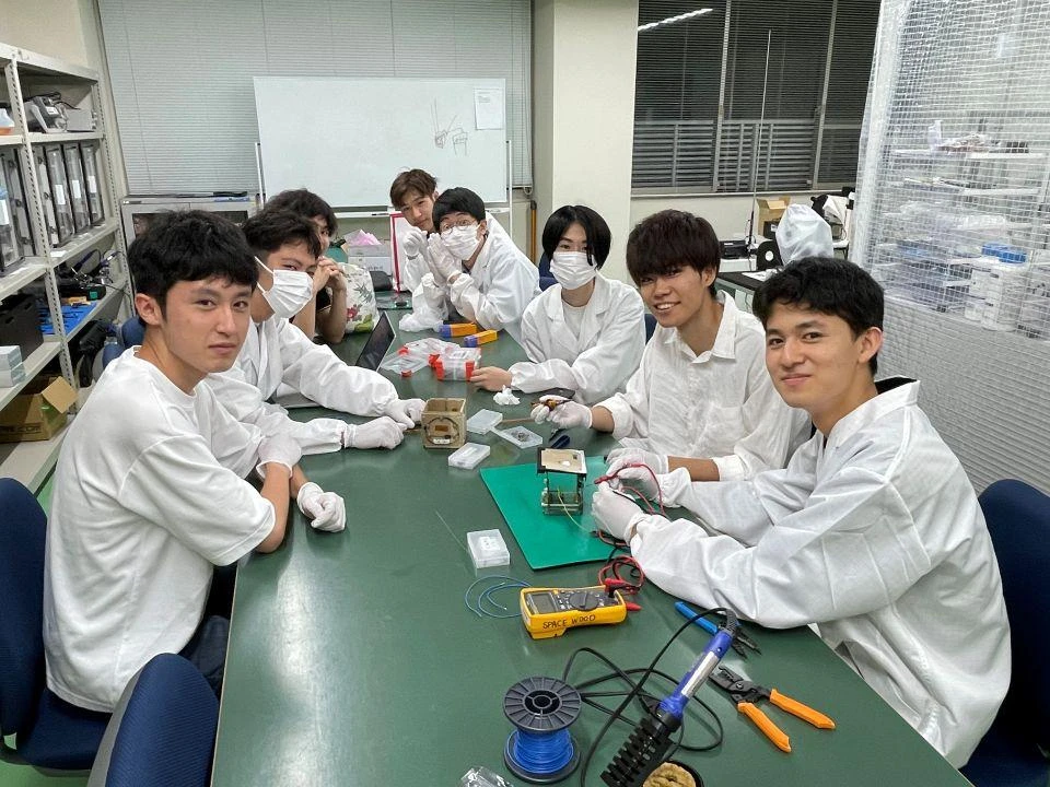 The student team from Kyoto University’s Space Wood Project sitting around a table working on the wooden satellite
