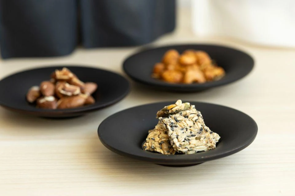 Three black plates with crackers and nuts with Ninja Paste
