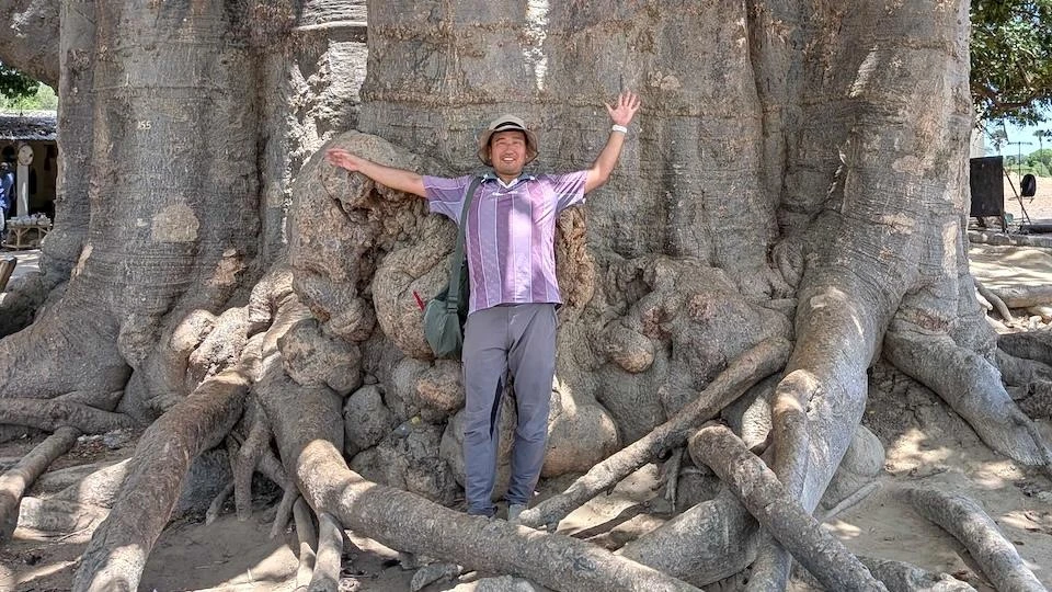 Funahashi Masatoshi, standing with his arms outstretched in front of a giant tree
